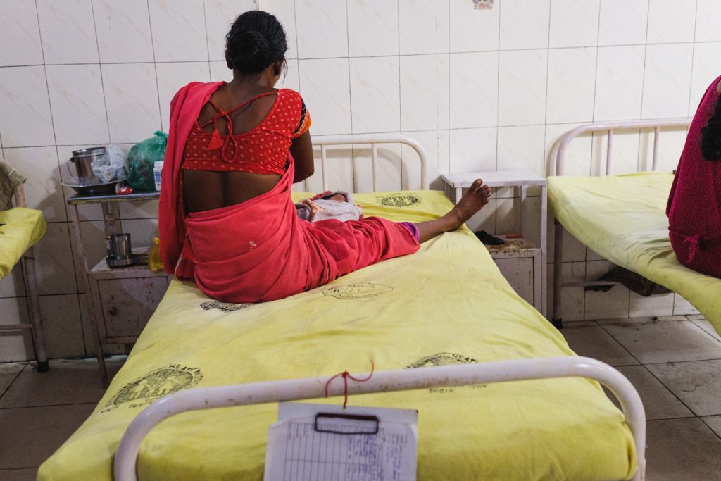 A young woman with her newborn baby sitting on a hospital bed in Bihar.