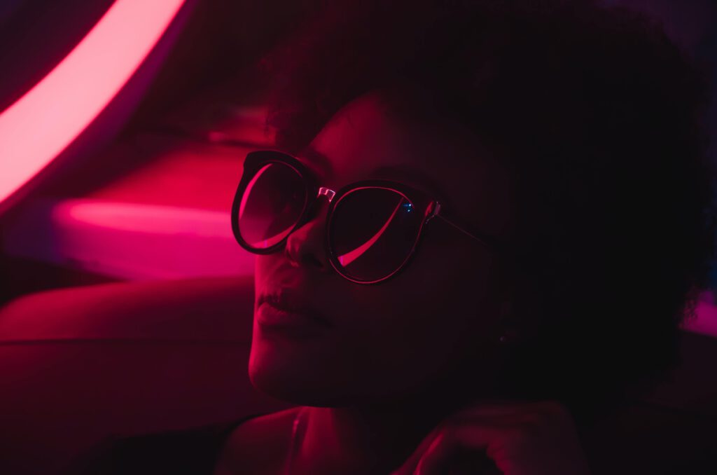 Kenya in 2030 builds alternative future scenarios. A Kenyan lady wearing sunglasses in a dark space with a pink background surrounded by a neon glow portrays a futuristic feel.