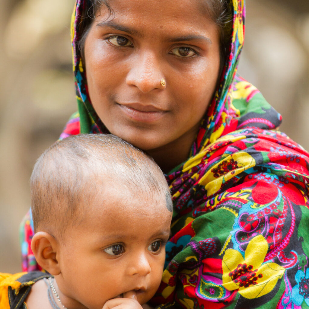 A Bangladeshi woman holding a small, approximately one year old child on her lap.