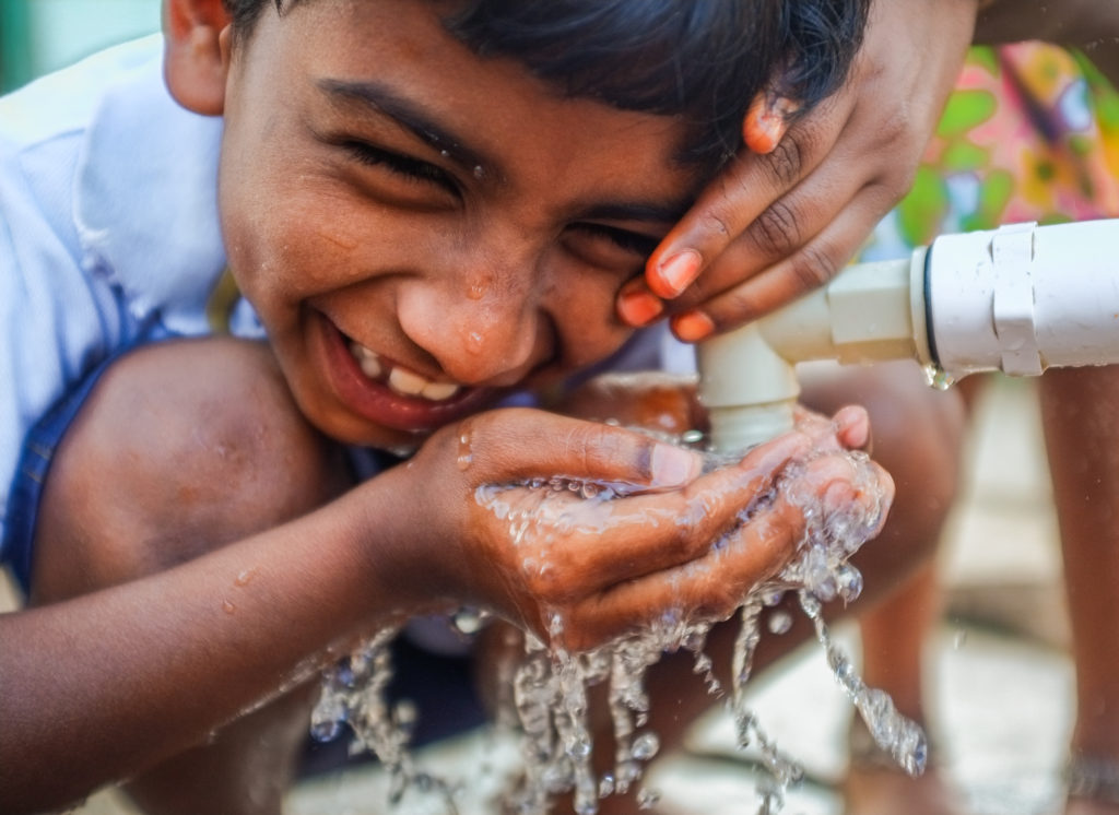 NISHTHA project WASH integration promotes healthy hygiene practices. A 10-year old boy laughing while washing hands at a water tap in India.